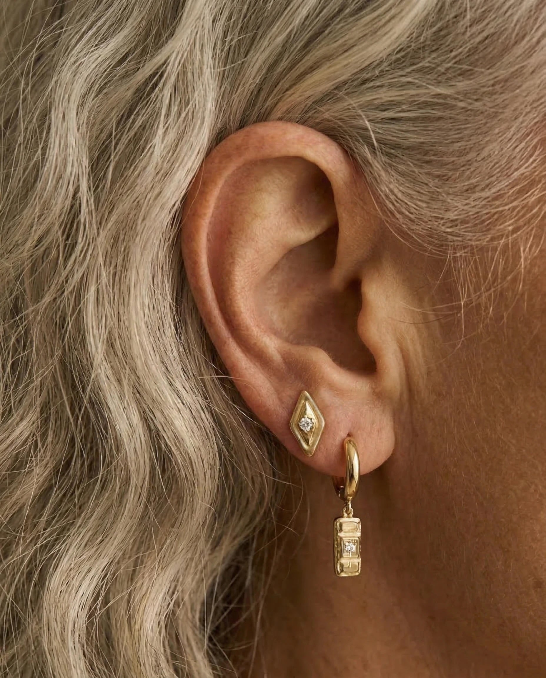 Close-up of an ear wearing gold hoop earrings with a diamond accent.